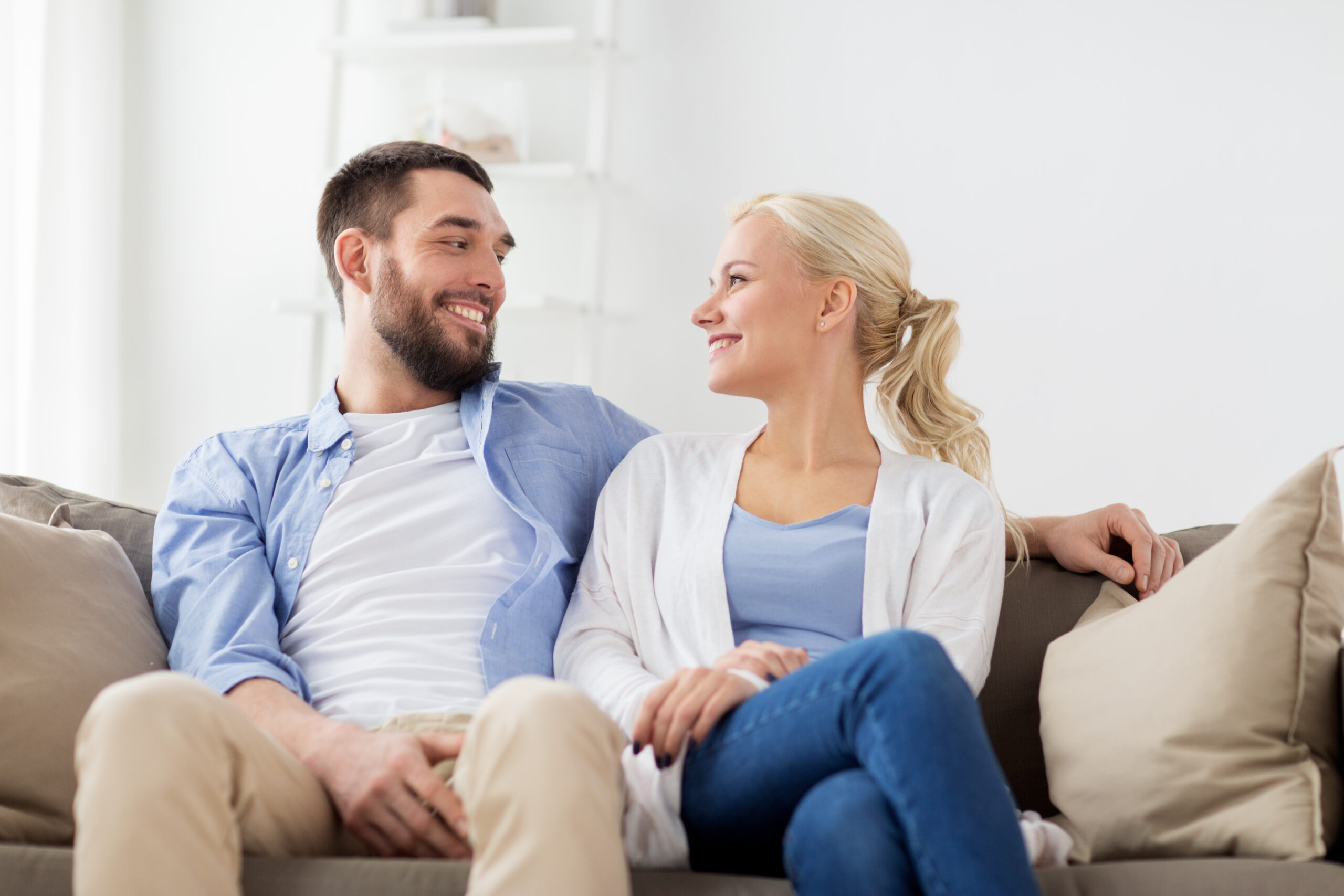 smiling happy couple sitting on sofa at home love, family and people concept - smiling happy couple sitting on sofa at home