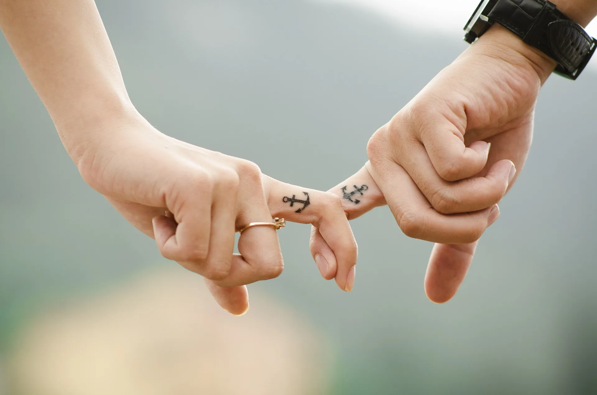 Two people linking pinky fingers with matching anchor tattoos and rings