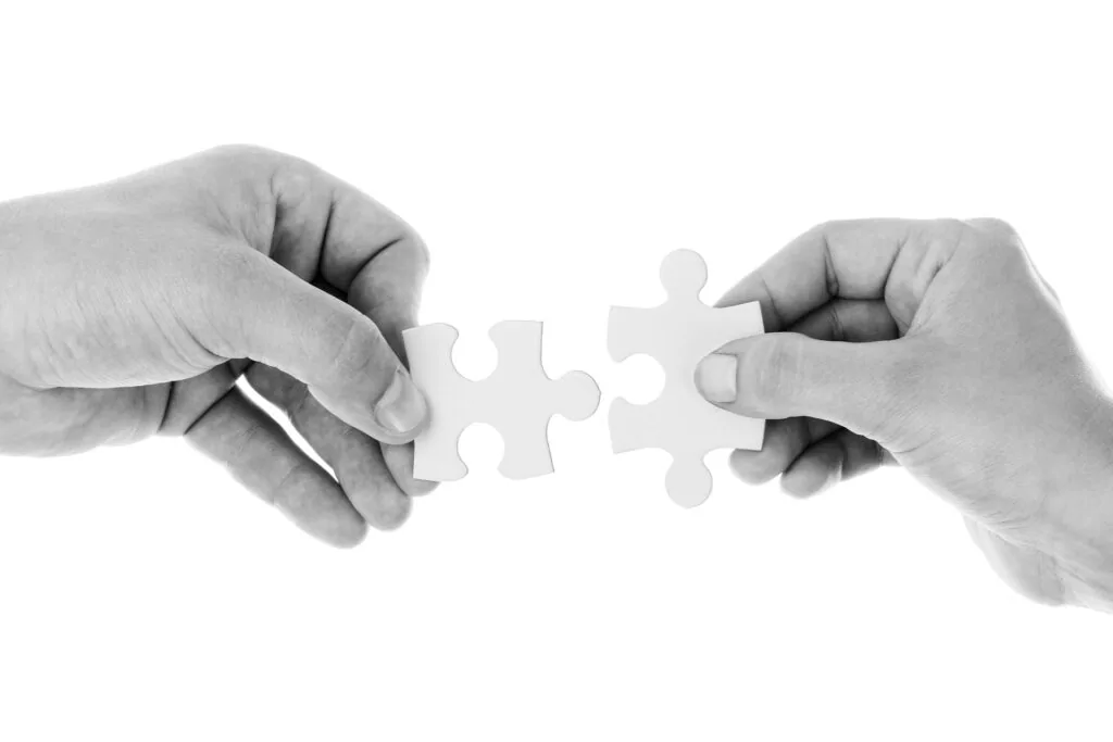 Two hands connecting puzzle pieces together in black and white