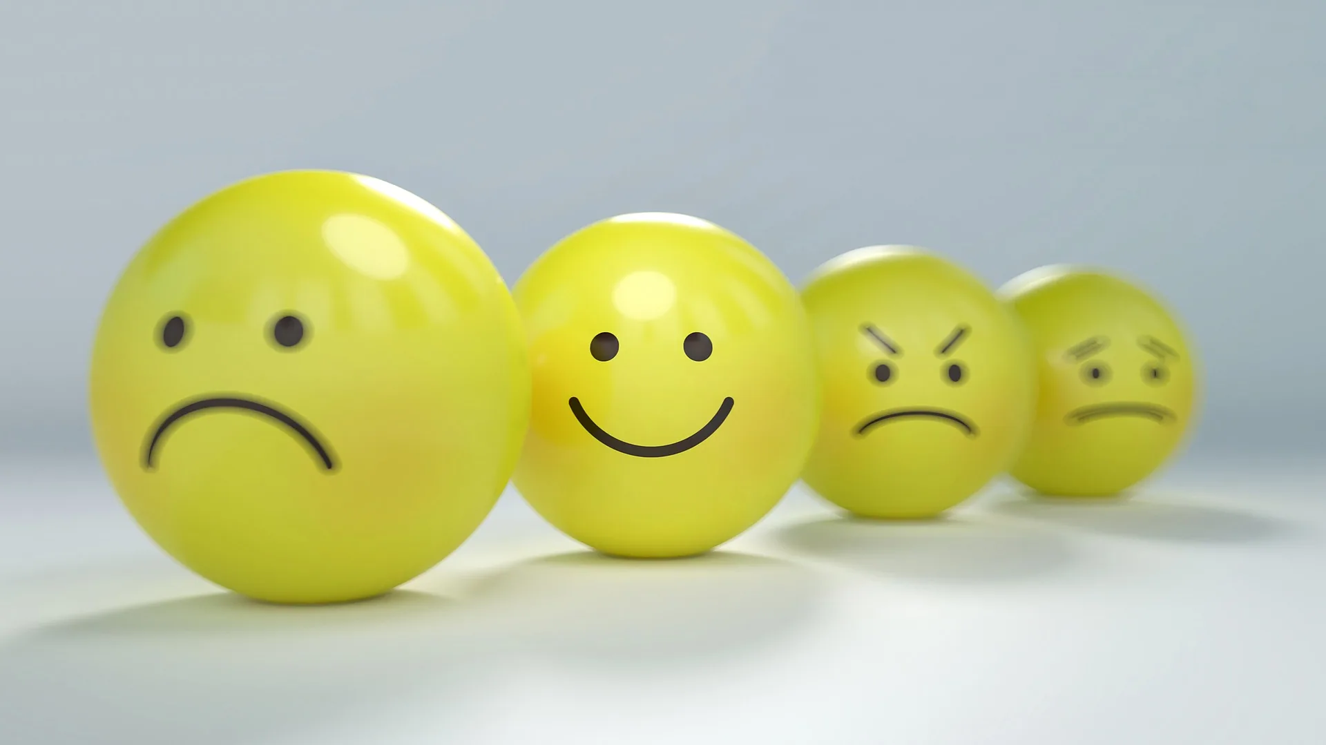 Four yellow spheres with drawn faces showing sad, happy, angry, and neutral expressions